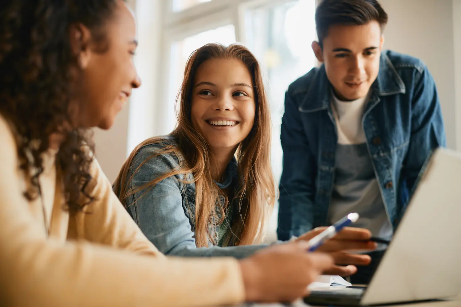 Fröhliche Gruppe von Gymnasiasten beim E-Learning am Laptop im Klassenzimmer.